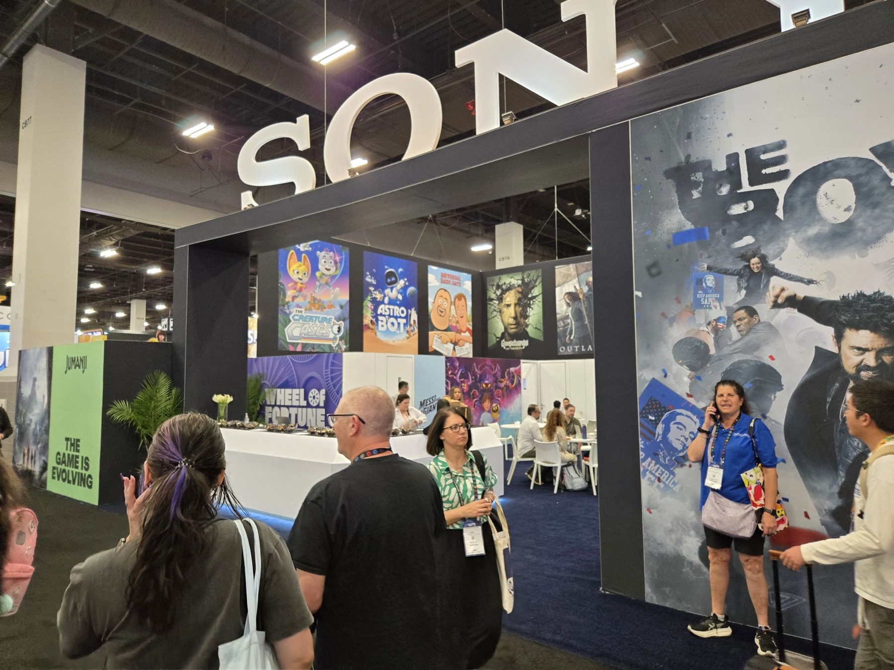 Sony booth wall with game and film posters, including The Boys, with attendees in conversation in front of it.